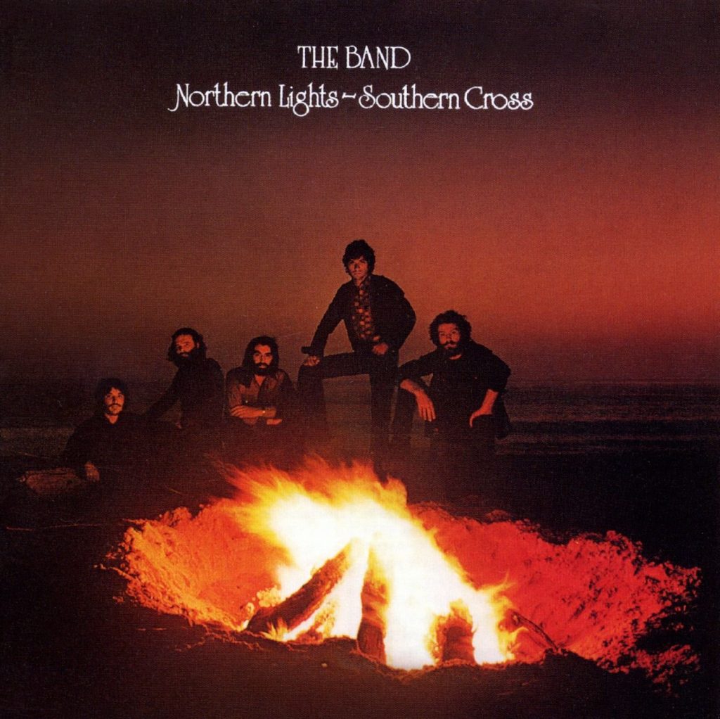 The album cover for Northern Lights-Southern Cross by The Band. Five pale-skinned men sit around a bonfire at night. The flames tinge the night sky orange.