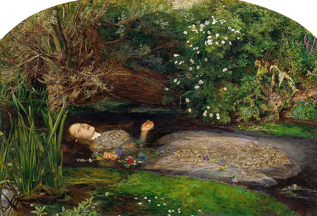 The 1851 painting Ophelia by John Everett Millais. A young woman with pale skin and golden brown hair wears a white gown with gold embroidery and lies partially submerged in a brook with her face up. In one hand, she loosely holds a garland of multicolored flowers. There are green bushes and a large brown tree trunk at the water's edge. Some grasses grow out of the water.
