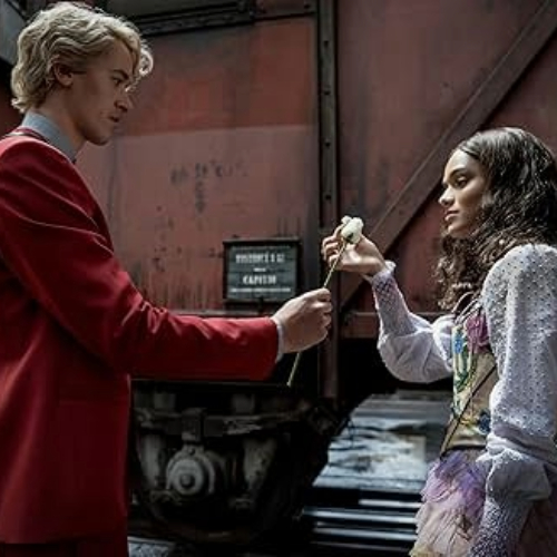 Movie still from The Ballad of Songbirds and Snakes, Snow handing Lucy Gray Baird a white rose.