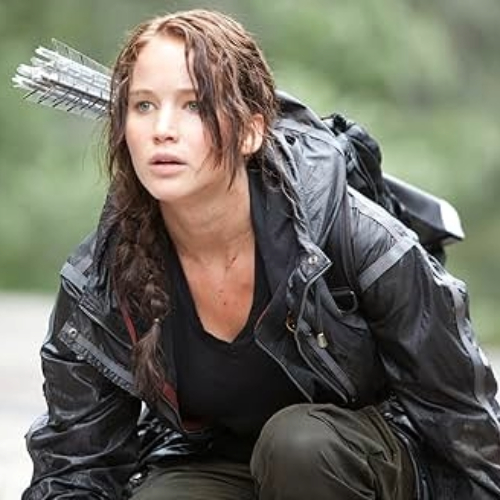 Movie still of Katniss Everdeen in the first Hunger Games movie, crouched down with a sheath of arrows on her back,