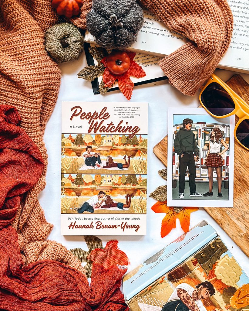 Flatlay picture designed by Bookstagrammer Britt of the romance novel People Watching by Hannah Bonan-Young. The book cover is centered with character cover art next to it with two orange sweaters, yellow sunglasses, fake leaves and fake pumpkins with open books decorating the background.