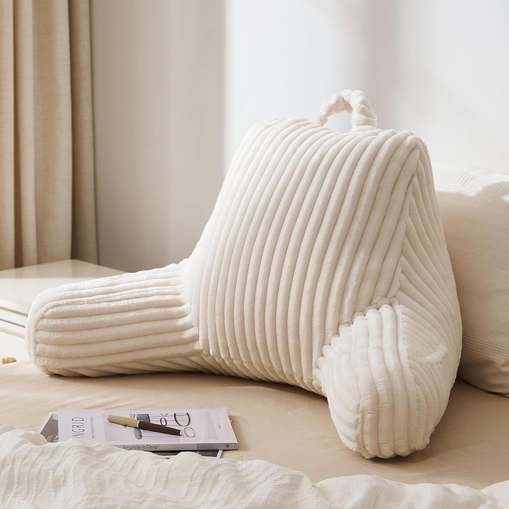 The image features a cream-colored backrest pillow on the floor with a paper and pen in front of it, with a blanket and curtains in the background.