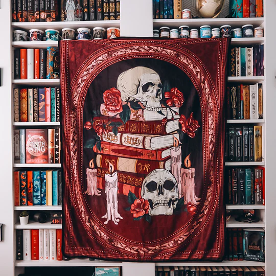 The image features a blanket set in front of full bookshelves. The blanket itself is two skulls with roses on top of books with two candles on the sides, they are surrounded by a mirror frame.
