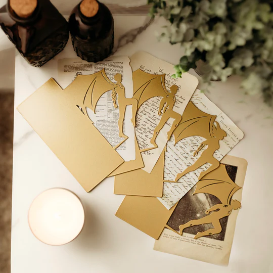 The image is of four book insets of winged characters, under them are torn pages from a book, a candle with bottles and greenery in the background.
