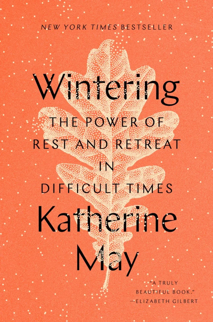 Wintering by Katherine May, a self-help book cover depicting a salmon-colored background with a white leaf in the center. The title is written in black letters.