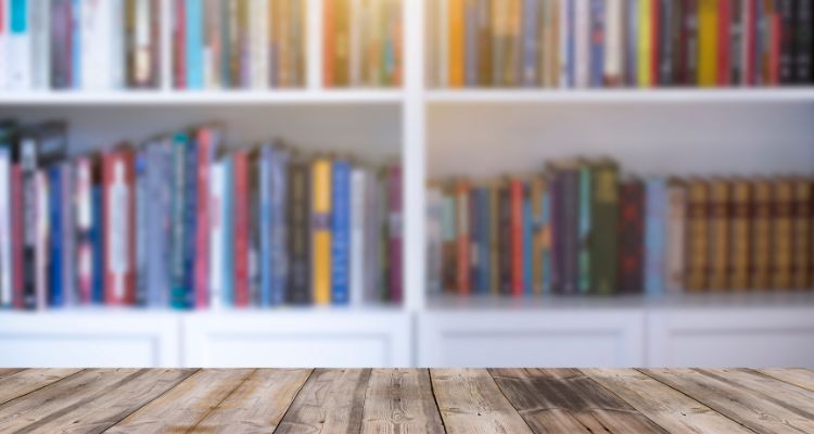 This image features white bookshelves with books and a wooden table in front of them.