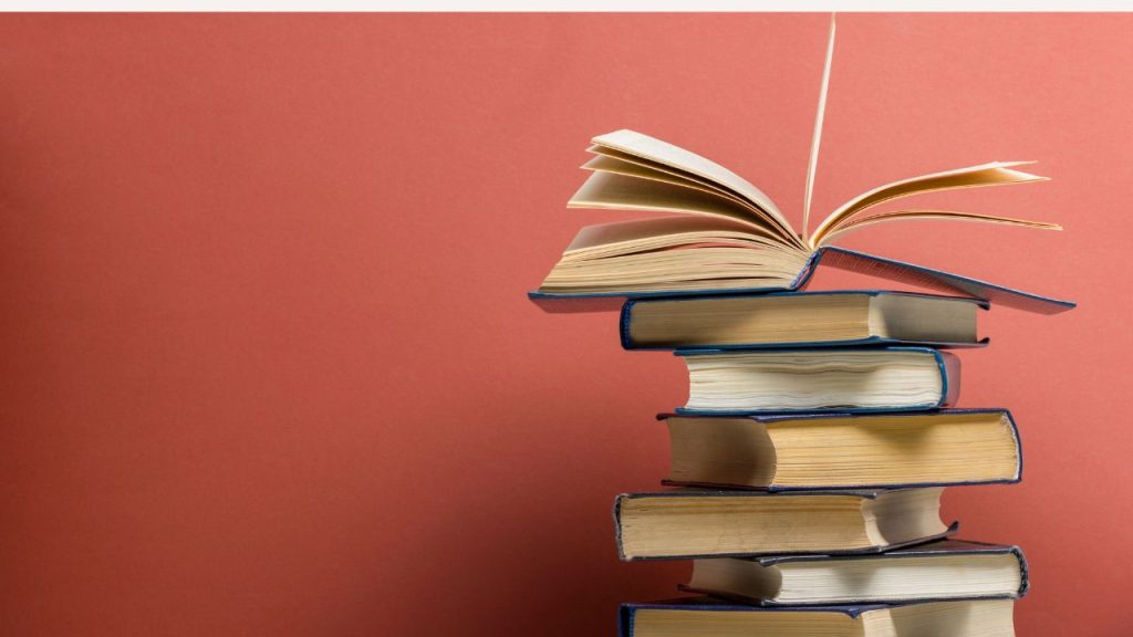 A misaligned stack of books with one book sitting open on the top, on a red background.
