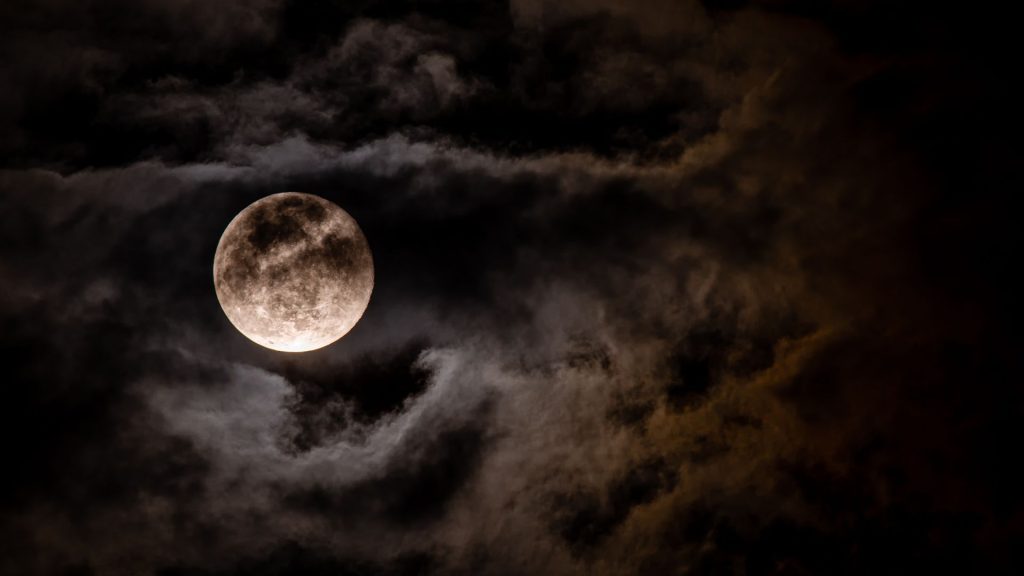 Full moon illuminating dark, swirling clouds in a night sky, creating a mysterious and dramatic atmosphere.