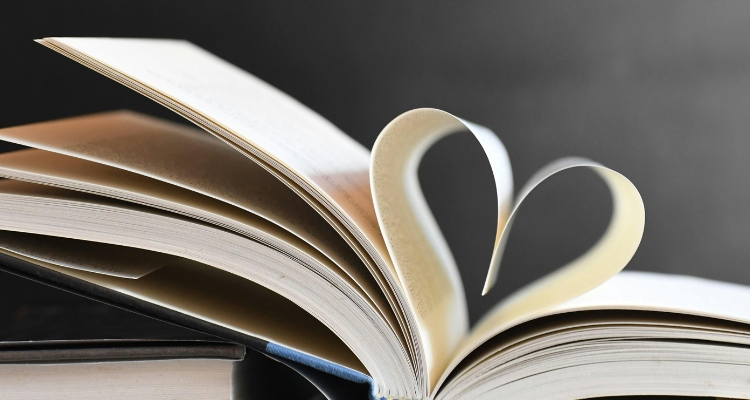 Open book with pages curved into a heart shape against a gray background.