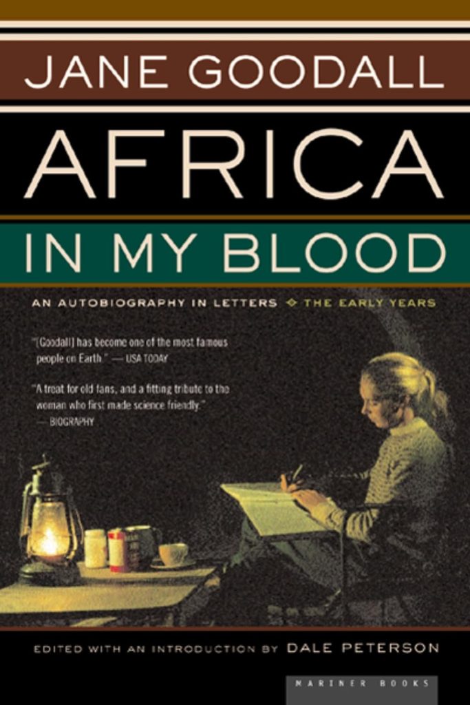 Africa in My Blood by autobiography by environmentalist Jane Goodall book cover depicts Goodall seated outside at a table, writing in a notebook by lantern.