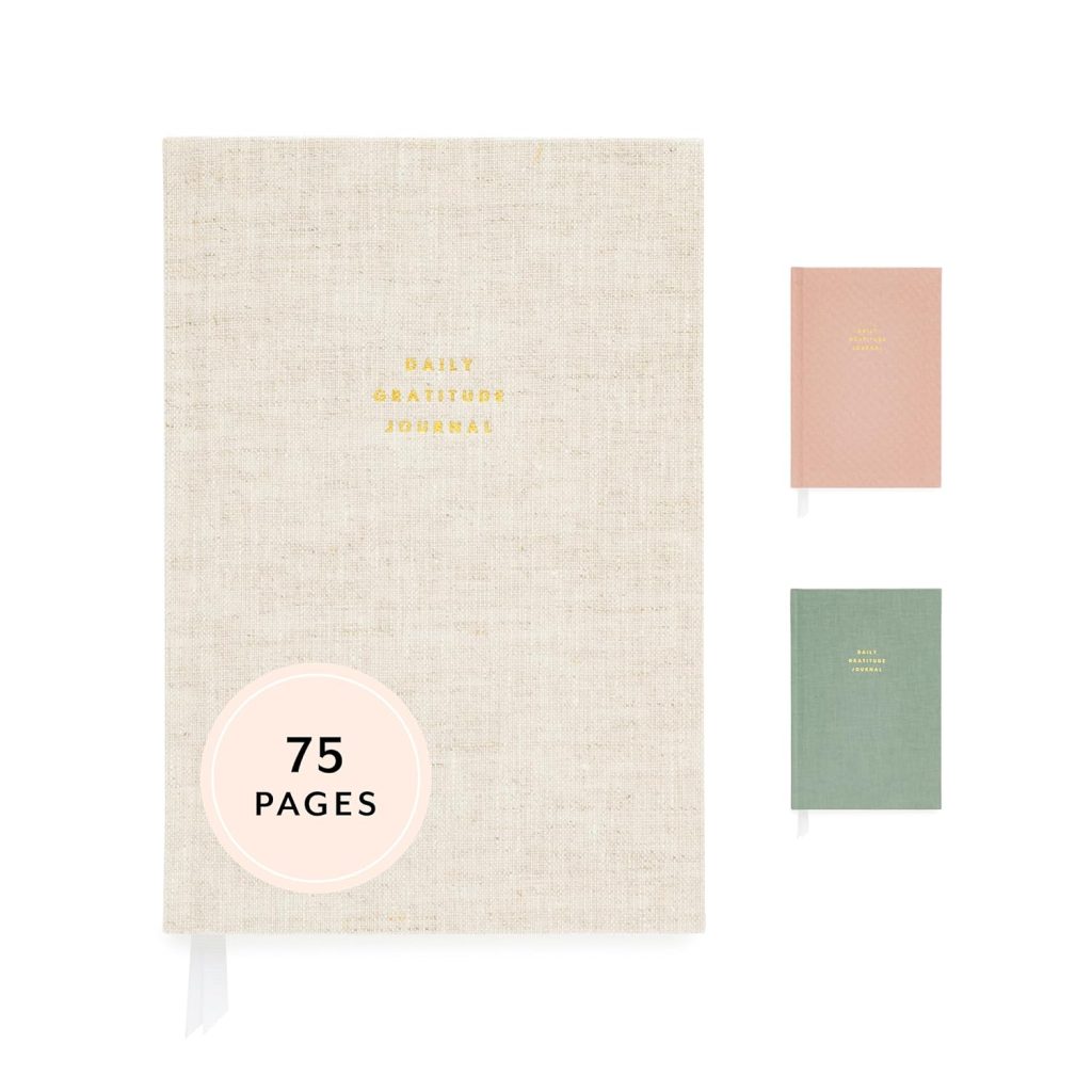 Sugar Paper's Daily Gratitude Journal with a hard copy cover with the title "Daily Gratitude Journal" in small gold font in the middle against a beige background. Next to it are two smaller journals, one with a coral cover and another with a green cover.