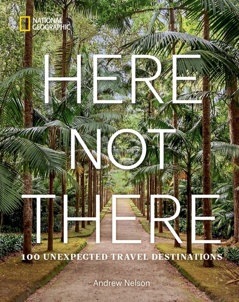 Here Not There: 100 Unexpected Travel Destinations by Andrew Nelson features rows of palm trees with a lined dirt path down the middle. Over top of the trees and path is the title and National Geographic in the top corner of the cover.
