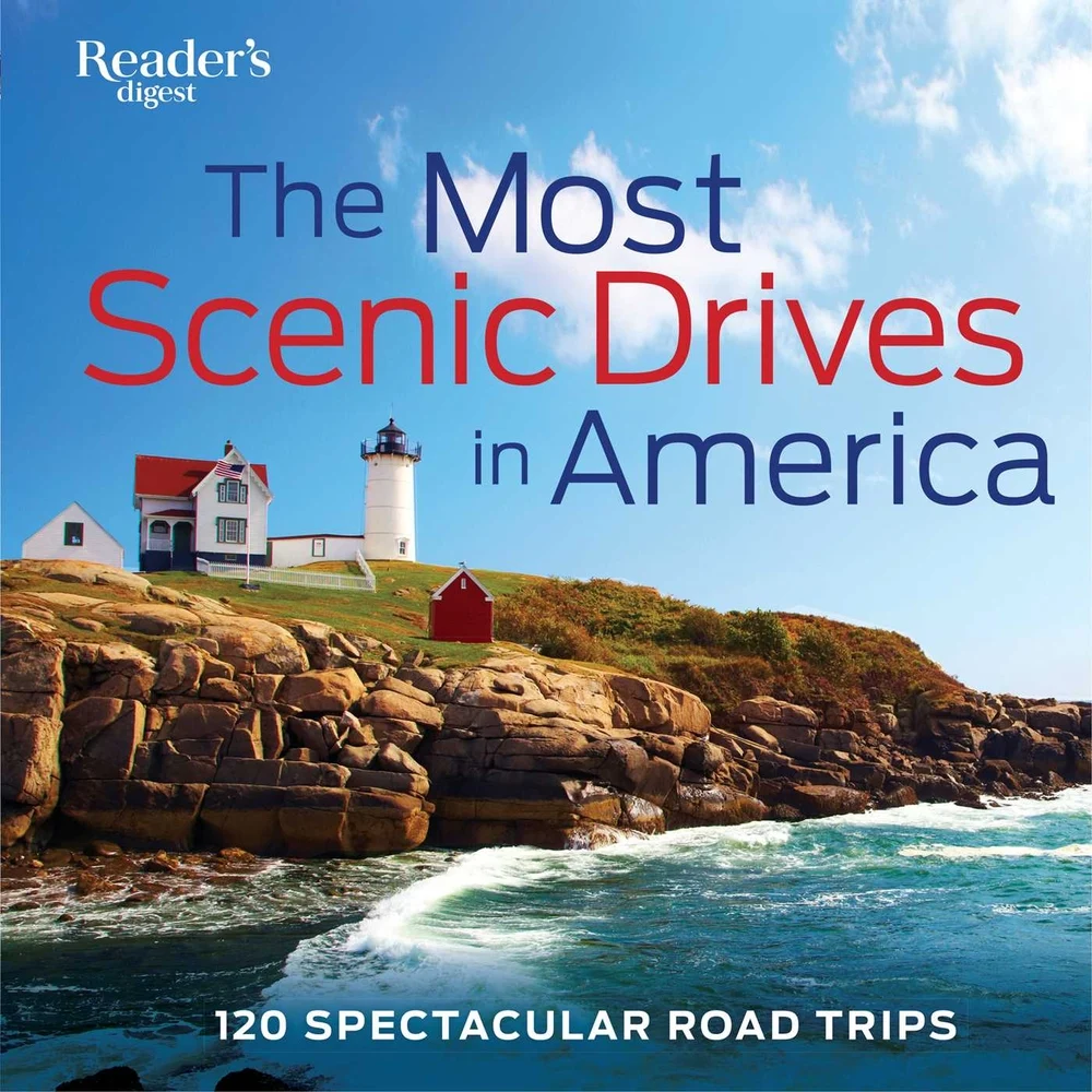 The Most Scenic Drives in America: 120 Spectacular Road Trips by Reader’s Digest features an island with a lighthouse and little house next to it close to the edge. The island is next to the ocean with crashing waves up against it.