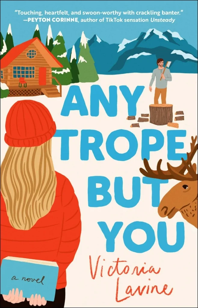 Any Trope But You by Victoria Lavine, a cozy romance cover showing a woman in a red jacket and beanie holding a book while facing a snowy cabin and mountain backdrop. A moose and a man chopping wood at a log appear nearby, highlighting the warm, whimsical tone.