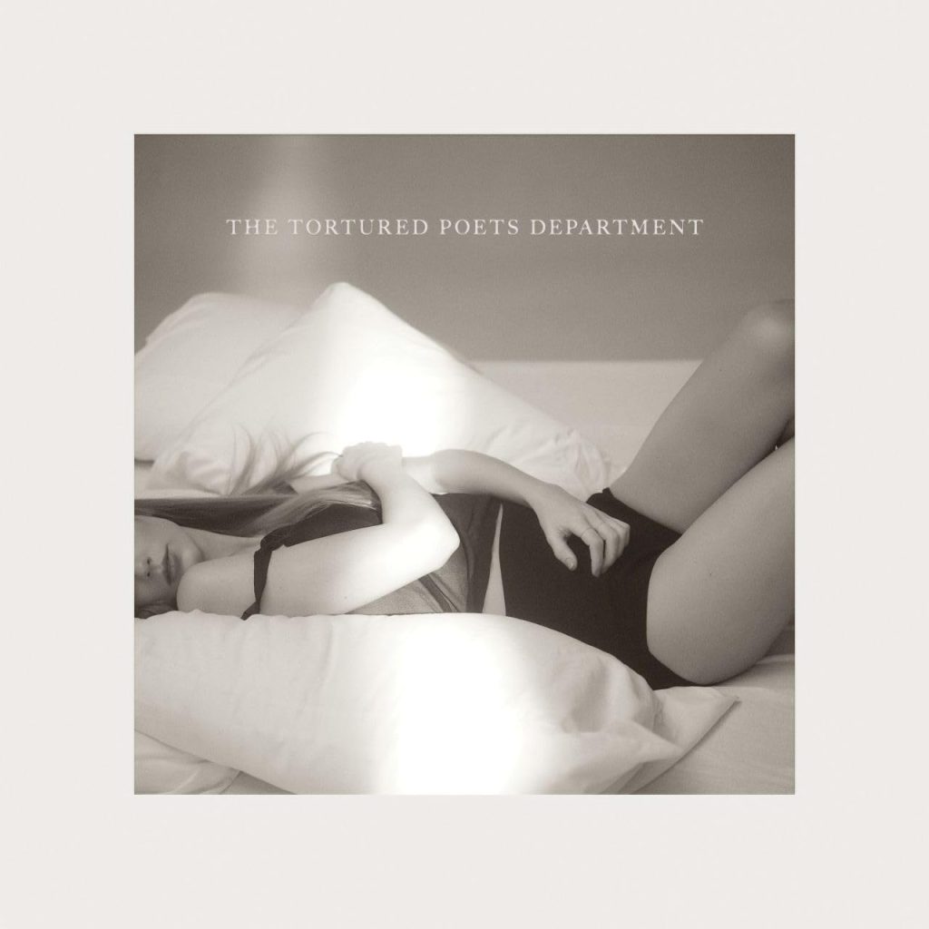 The album cover for The Tortured Poets Department by Taylor Swift. Featured in black and white, Taylor Swift wears black lingerie and lounges on top of white pillows and white sheets.