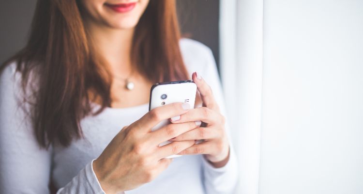 A light skinned dark haired woman holding a white smart phone.
