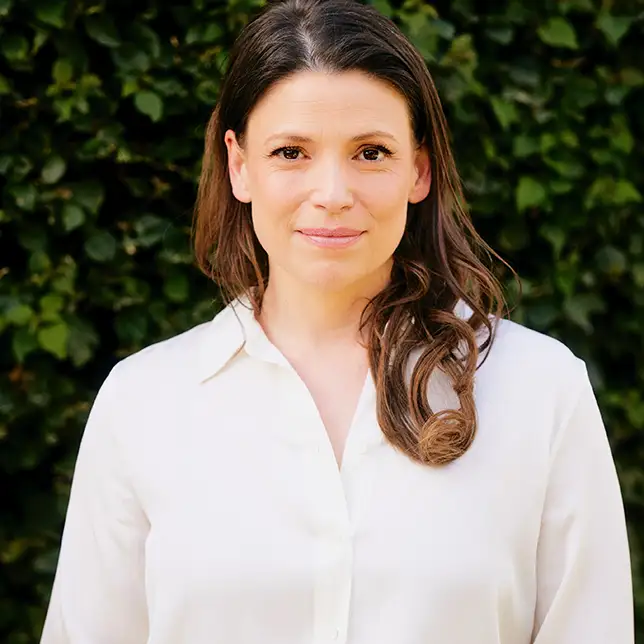 Author and audiobook narrator Julia whelan stands outside before greenery wearing a white button up.