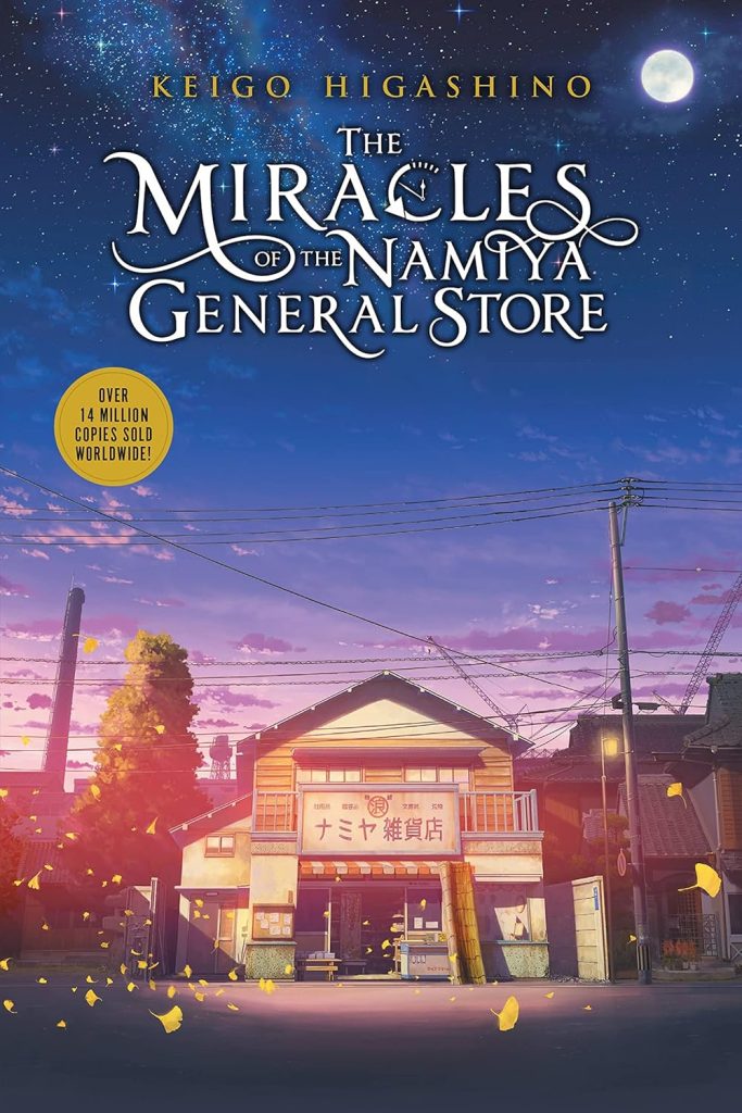 The Miracles of the Namiya General Store by Keigo Higashino, a fiction novel cover depicting an illustrated two-story Japanese general store on a street at dusk. Yellow gingko leaves float across the cover, and power lines cross the lower part of the blue and pink sky.