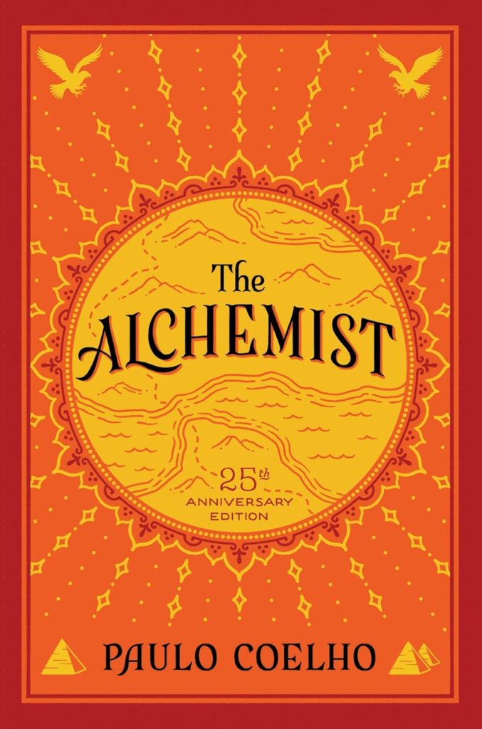 The Alchemist by Paulo Coelho, a fiction novel cover in orange and yellow. The title is in aa yellow/light orange circle that has a border around it and geographical lines of rivers inside, and lines of diamonds radiate out from the circle's borders. Two birds sit in the top corners, and pyramids sit in the bottom corners.