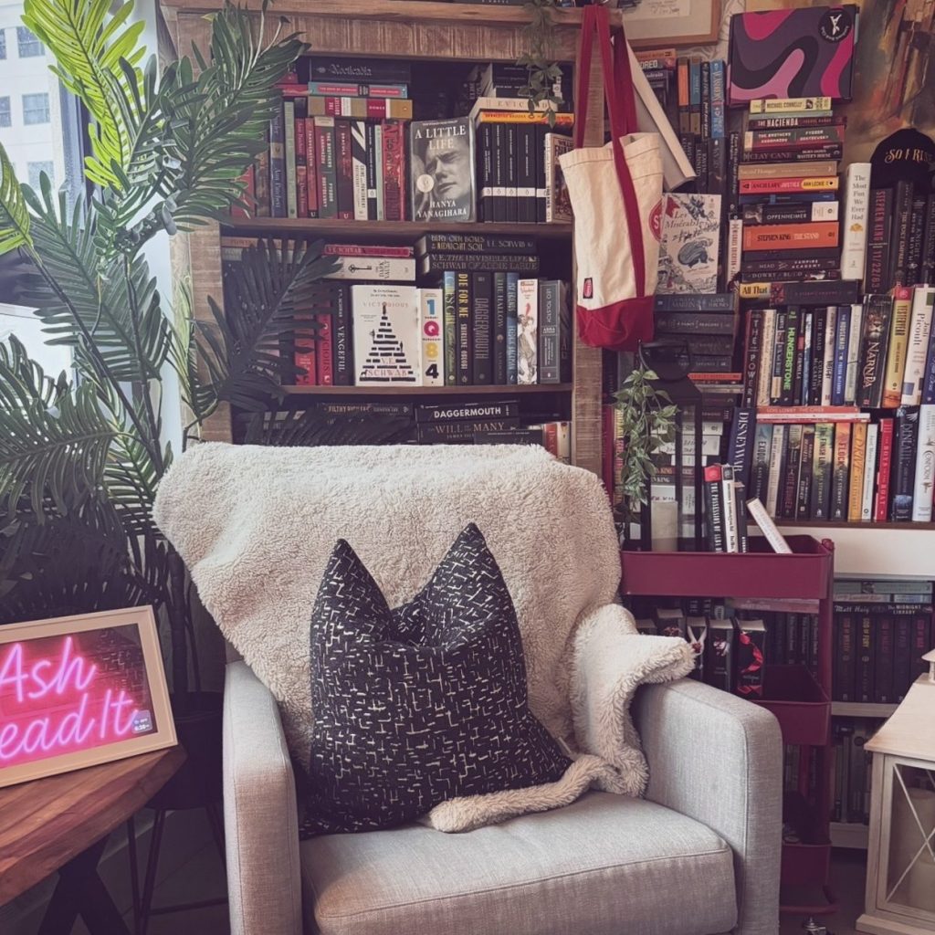 Bookstagrammer Ashley Lauren's book nook featuring a chair with pillow and blanket before book filled shelves.